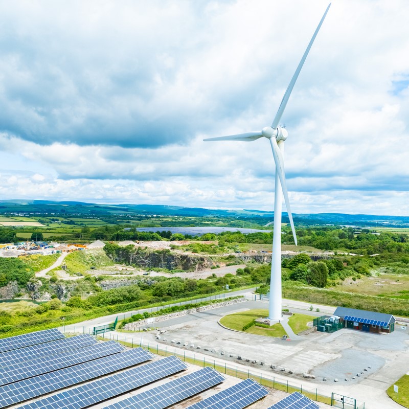 erial view of solar panels and Wind turbines on green field at suburb in sunny day 