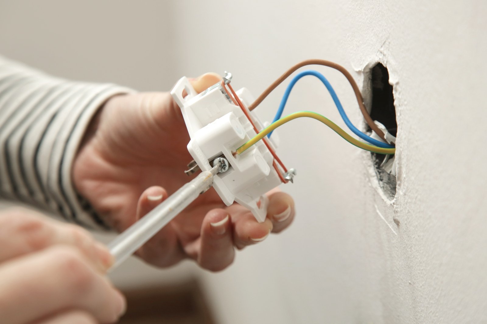 Image of an electrician removing a plug and showing the blue, brown and green/yellow wires
