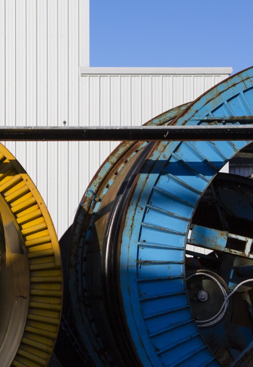 A close up of a large blue metal cable drum and a large yellow metal cable drum