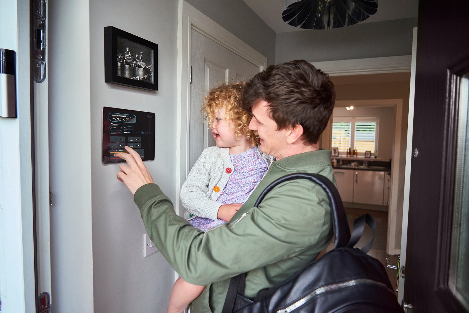 A man carrying a toddler as he changes the settings on a digital thermostat on the home