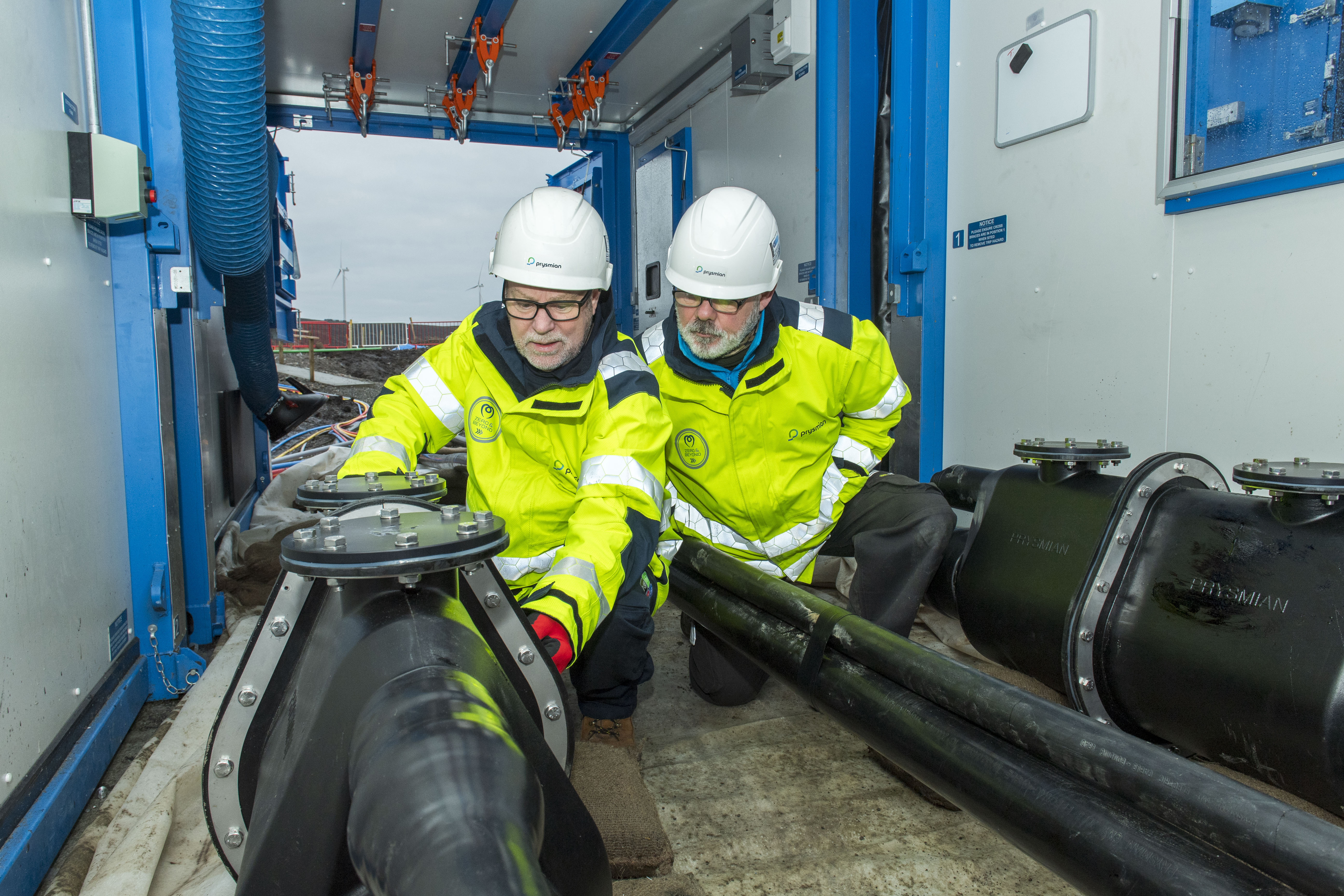 Two engineers looking at a large black high voltage cable on the ground