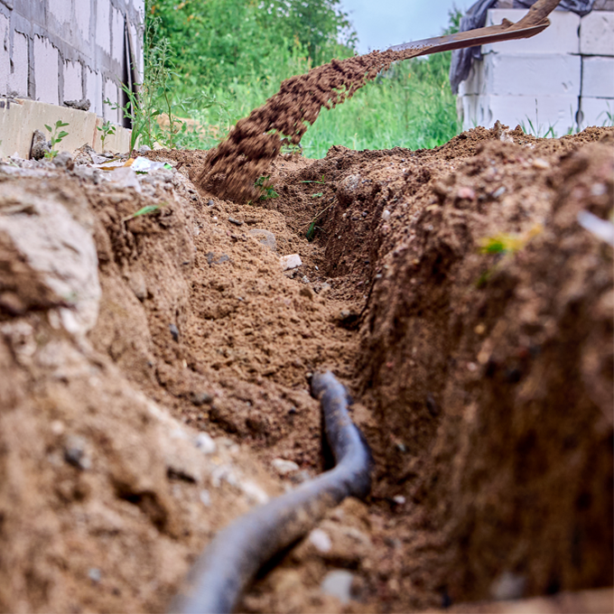 Construction worker is digging trench for laying cables, using shovel to excavate soil.