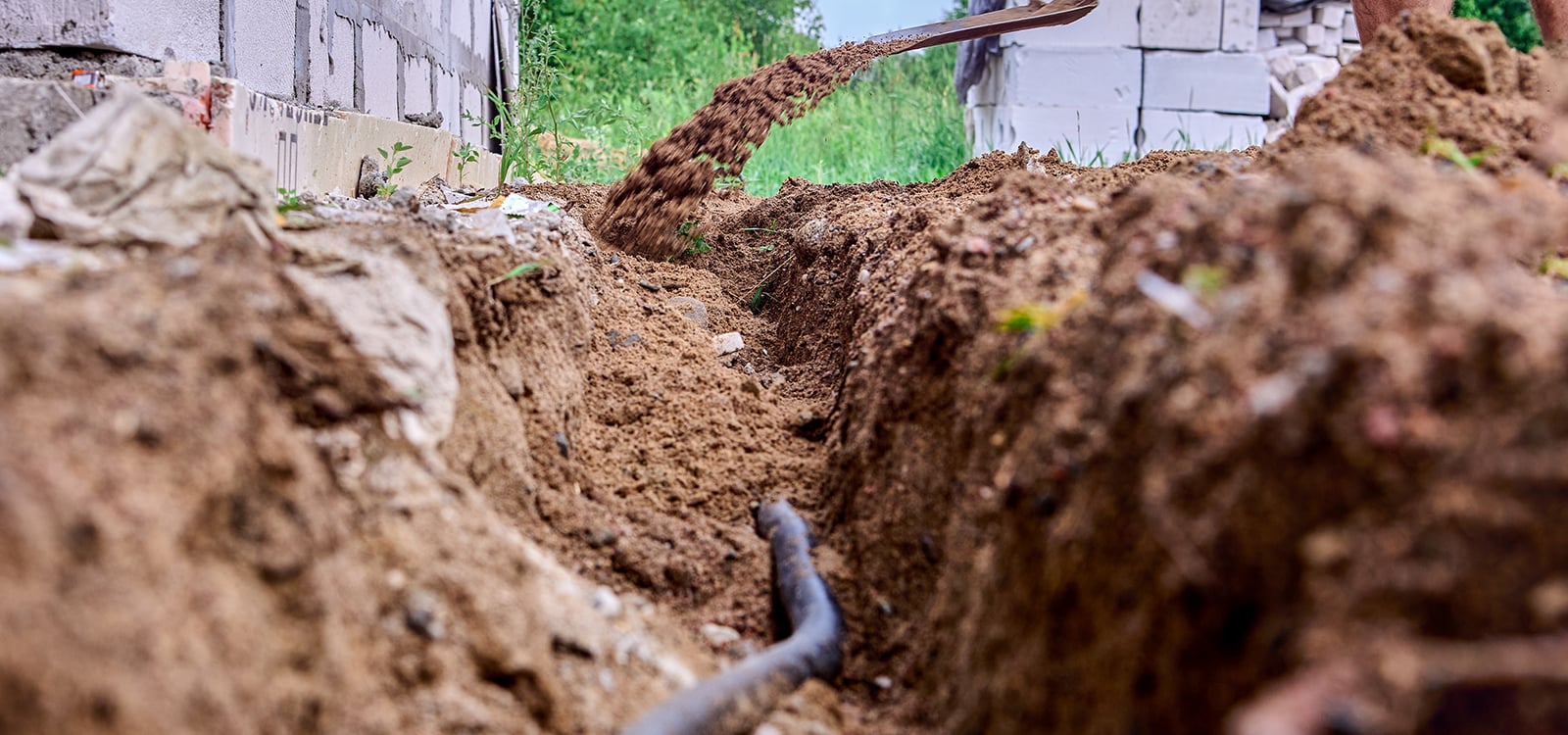 Digging trench for laying cable, construction worker uses shovel to take out soil.
