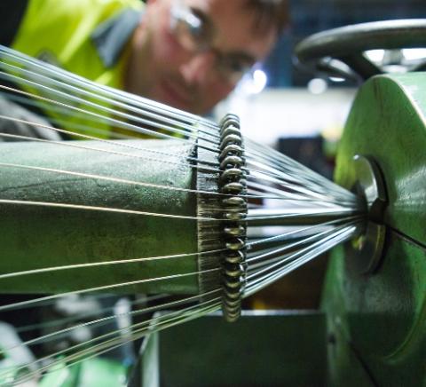 A worker looking at steel wire rotate on a stranding machine in a cable factory
